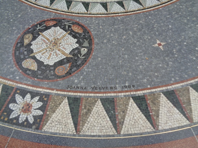 Close up of a name (the designer?) in the outer part of the large design surrounding a metal cover in County Arcade, Leeds (taken June 23 2016).